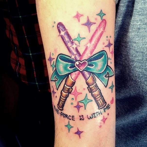 Romantic style colored little crossed lightsabers with bow tattoo on forearm stylized with stars and lettering