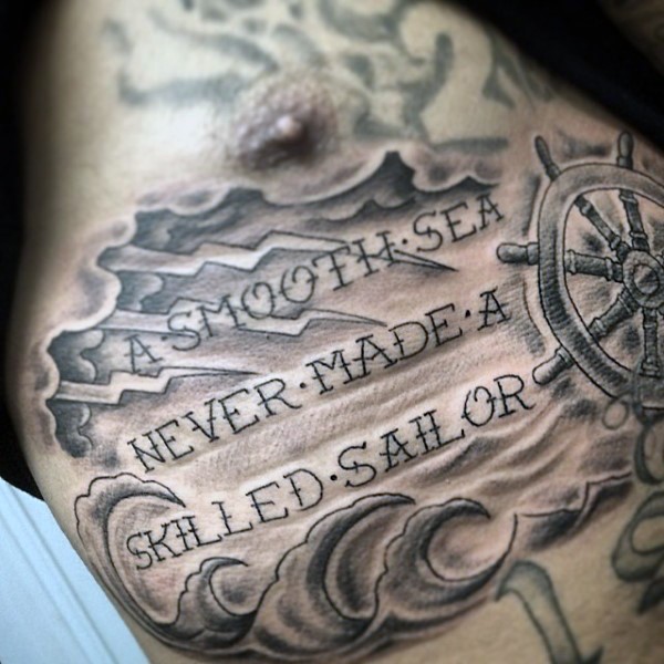 Romantic style nautical themed black ink tattoo with steering wheel and lettering on chest
