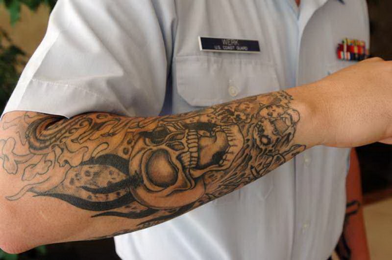 Tattoo von angsteinflößendem hornigem Totenkopf in Flammen in grauer Tusche als Ärmel gestaltet am Unterarm