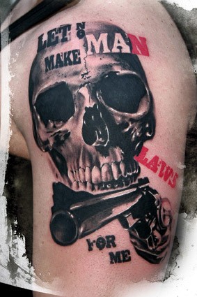 particolare disegno grande realistico cranio con lettere e pistola tatuaggio su spalla