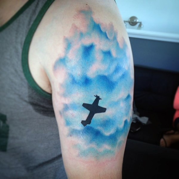 Tatuaje en el hombro, avión negro  pequeño en el cielo azul
