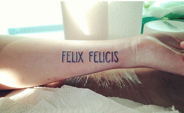 Simple black ink forearm tattoo of &quotFELIX FELICIS" lettering
