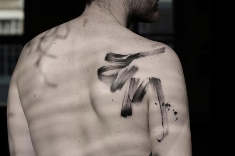 Simple black ink ribbon shaped tattoo on shoulder area