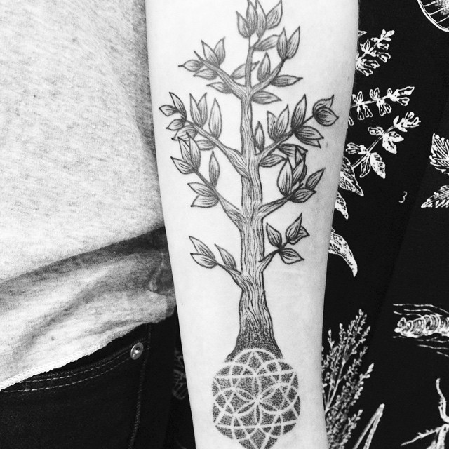 Simple black ink tree tattoo on forearm combined with ornamental flower