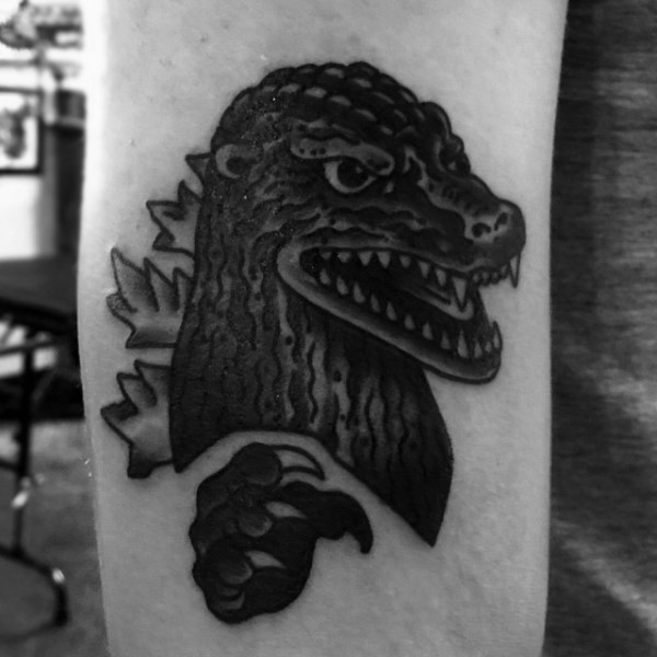 Simple cartoon like black ink little Godzilla head tattoo on arm