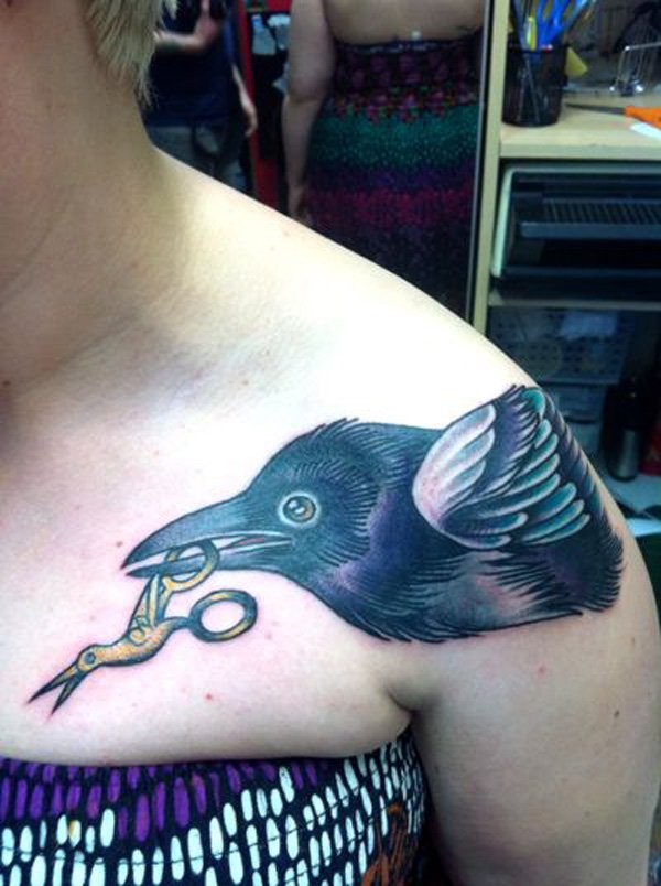 Simple cartoon like colored crow head tattoo on shoulder with bird shaped scissors