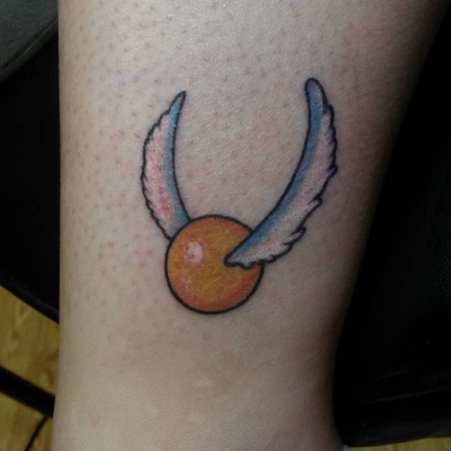 Simple cartoon like colored golden ball with wings tattoo