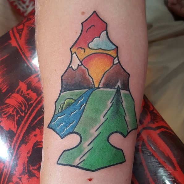 Simple colored vintage style antic arrow head tattoo on forearm stylized with mountain river