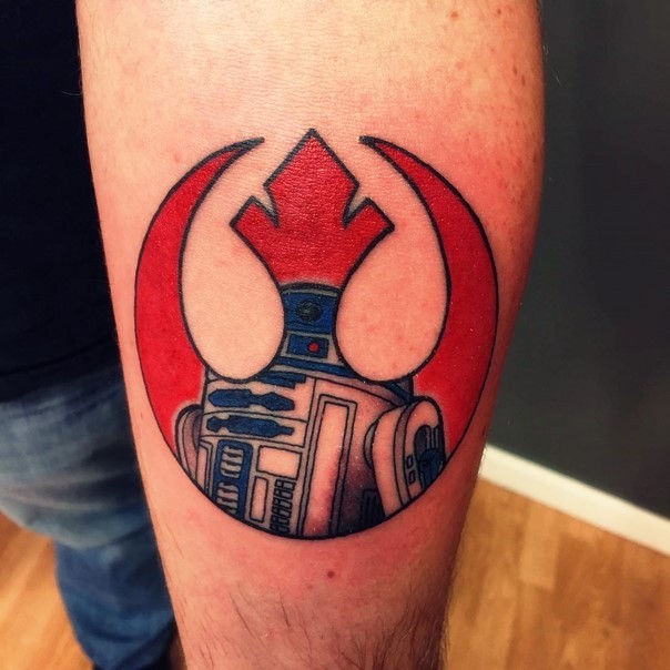 Tatuaje en el antebrazo,
 emblema de la alianza Rebelde de color rojo decorado con R2D2
