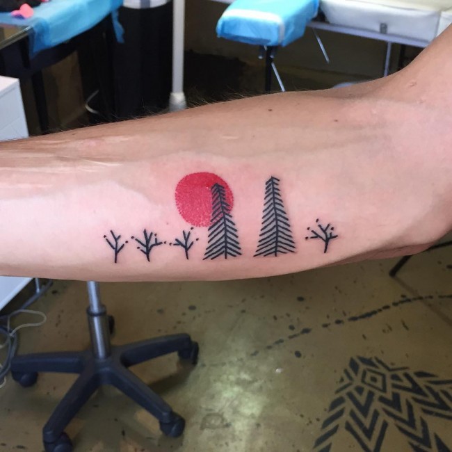 Simple homemade black ink tiny forest tattoo on forearm with red sun