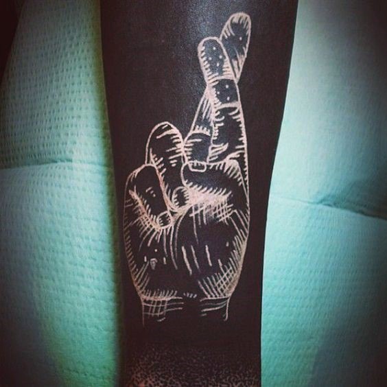Tatuaje en el antebrazo, mano blanco con dedos cruzados en el fondo negro
