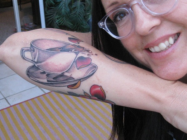 Simple old cartoon like colored coffee cup tattoo on forearm stylized with red hearts