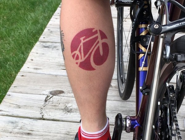 Simple red colored bicycle shaped emblem tattoo on leg