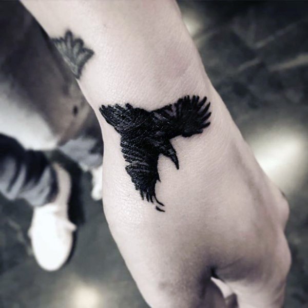Simple tiny black ink crow tattoo on wrist