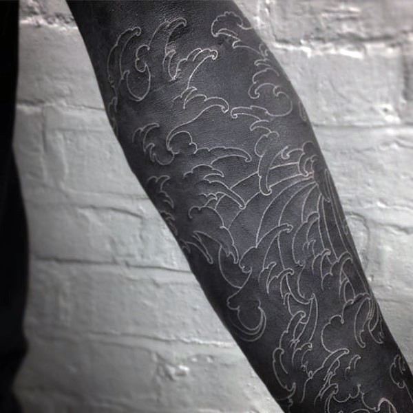 Tatuaje en el brazo, manga negra con olas dibujadas de tinta blanca