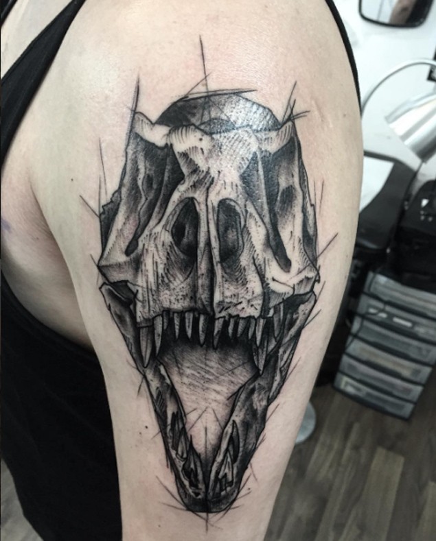 Sketch style black ink shoulder tattoo of dinosaur skull