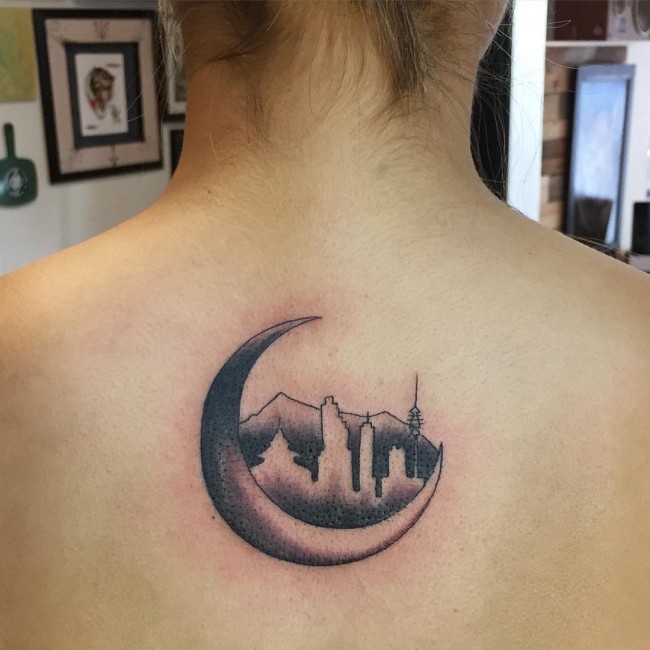 Kleines schwarzes und graues Tattoo am oberen Rücken mit der nächtlichen Stadt und Mond