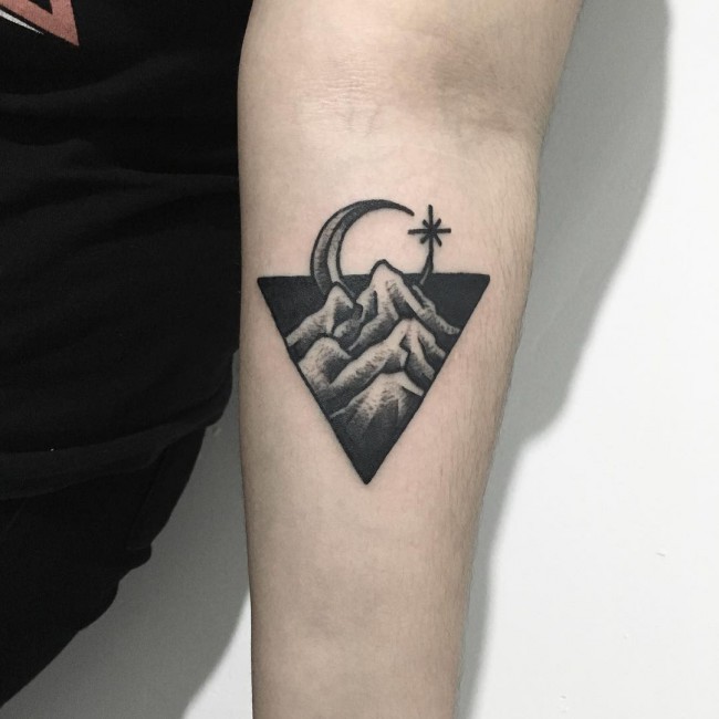 Small black ink triangle shaped forearm tattoo stylized with mountains and moon