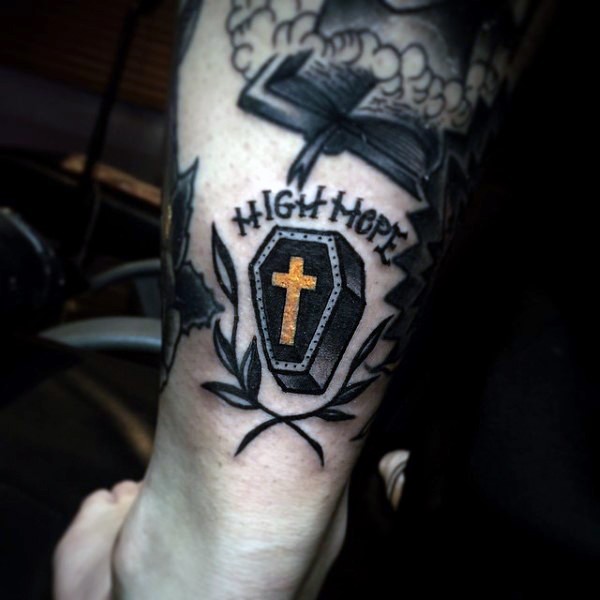 Tatuaje en la pierna, ataúd pequeño con cruz dorado y escrito