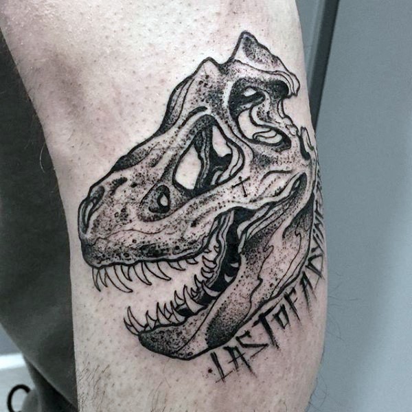 Small engraving style dinosaur skull with lettering tattoo on elbow