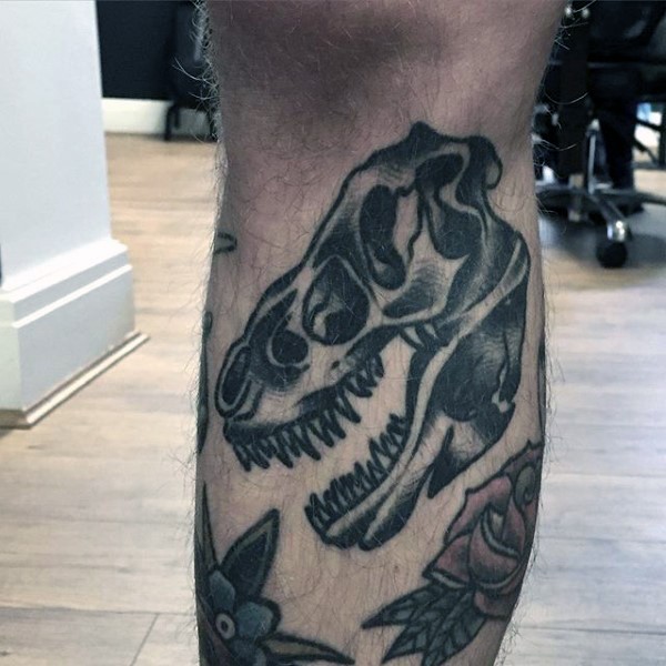 Small old school style black ink leg tattoo of dinosaur skull