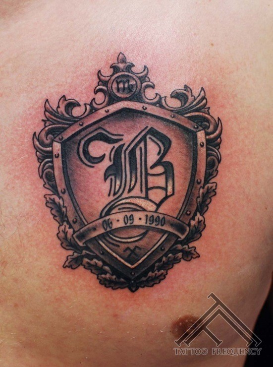 Small shield shaped chest tattoo of old symbol with lettering