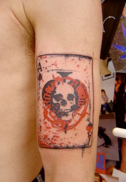 Small watercolor style arm tattoo of card stylized with skull