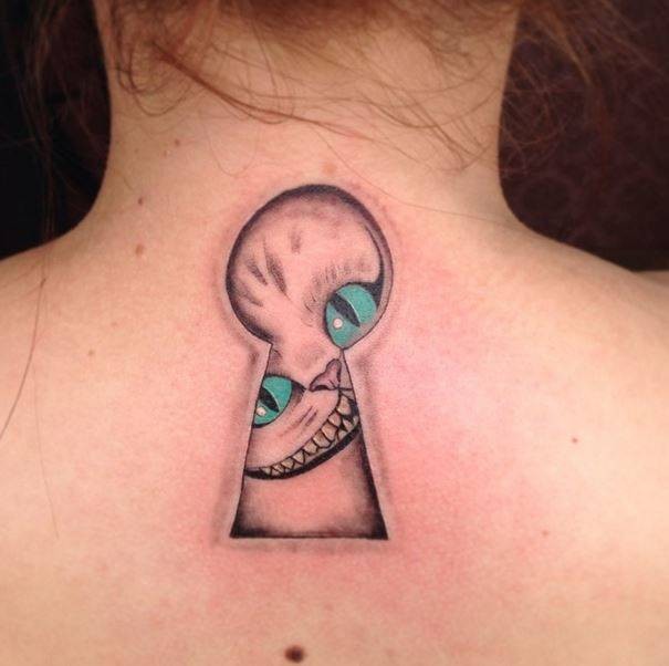 Smiling Cheshire cat looking into door slot upper back slightly colored tattoo