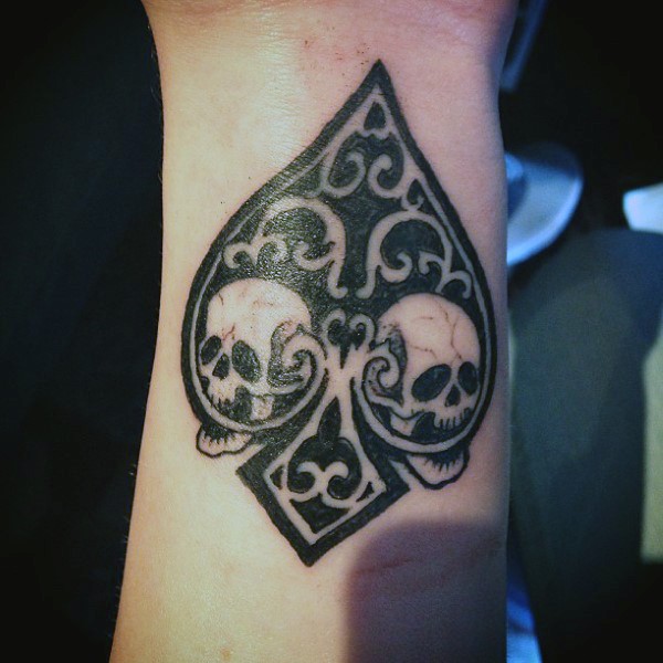 Spades symbol designed with skulls and ornaments black and white tattoo on wrist