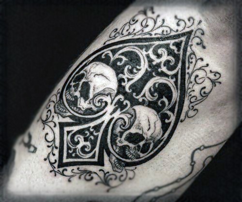 Tatuaje en el antebrazo, símbolo de naipes pica decorada con cráneos