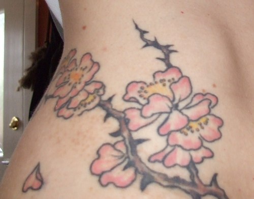 Tatuaje en la cadera, rama espinosa con flores de color rosa