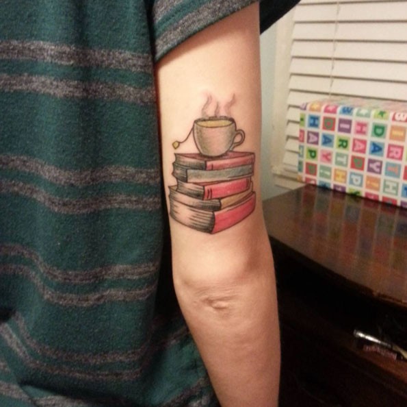 Steaming tea cup on pale of thick books colored arm tattoo