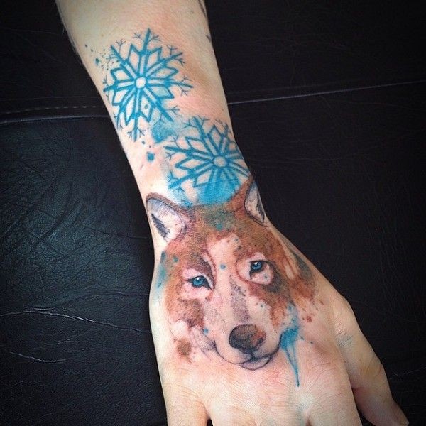 Stippling style colored wrist tattoo of wolf with snowflake