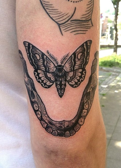 Tatuaje en el brazo, mandíbula humana con polilla, colores negro blanco