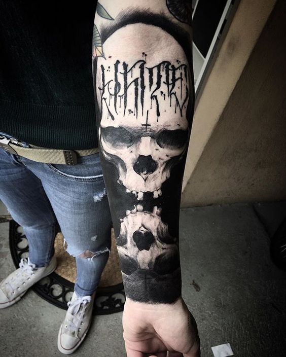Stunning blackwork style forearm tattoo of mirrored skulls with lettering