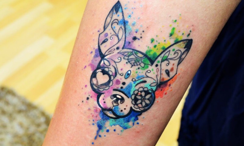 Stylized little dog's portrait with unusual eyes tattoo on forearm in watercolor style