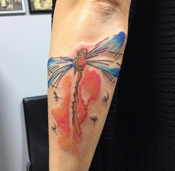 Stylized multicolored flying dragonfly forearm tattoo in watercolor style