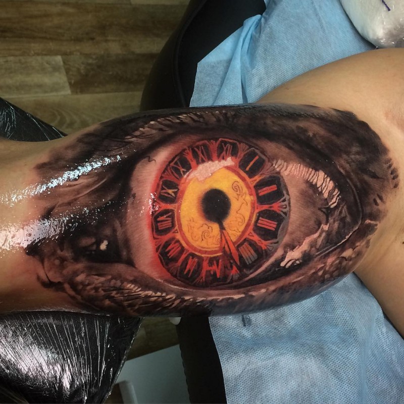 Superior multicolored biceps tattoo of eye stylized with clock