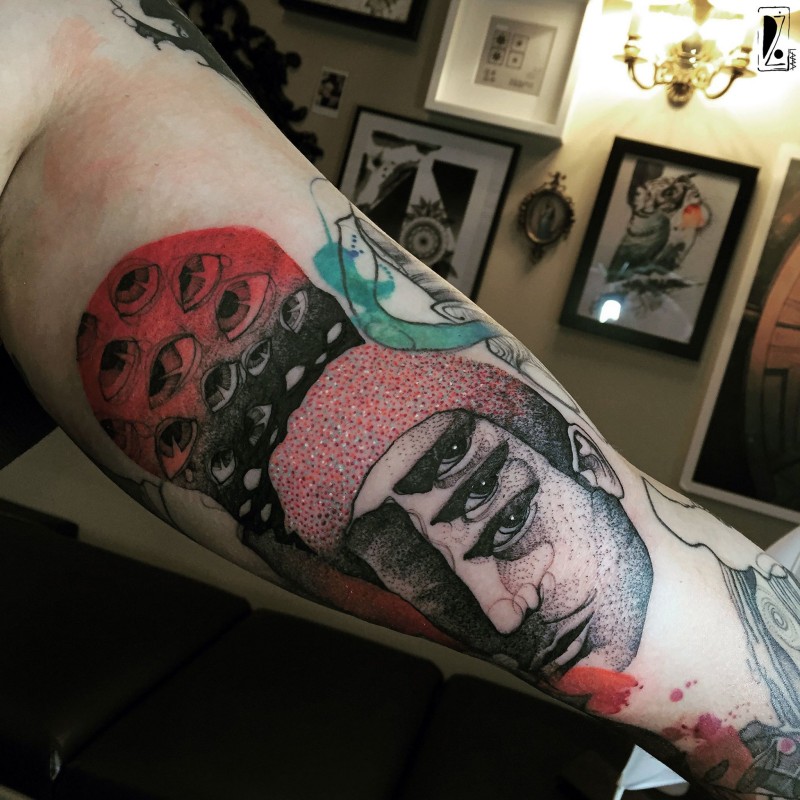 Surrealism colored biceps tattoo of creepy man face with eyes by Joanna Swirska
