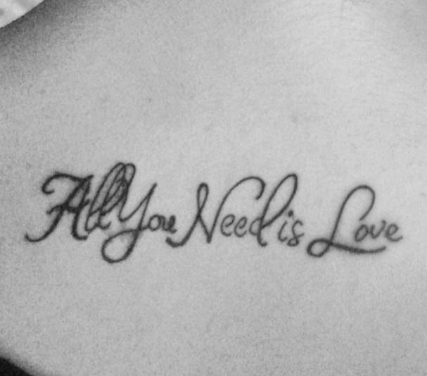 el tatuaje de la frase &quotall you need is love" &quotel amor es todo lo que necesitas" en cursivo hecho en la espalda