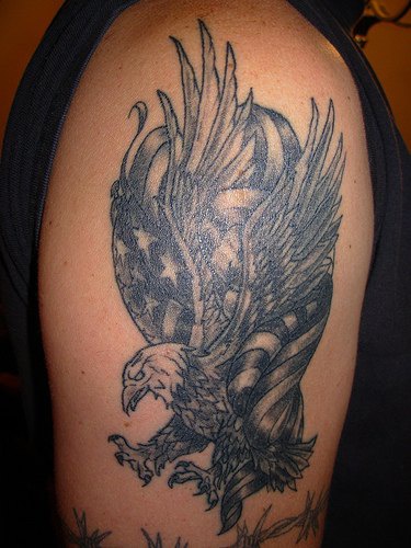 el tatuaje de tinta negra con una aguila y la bandera americana hecho en el hombro
