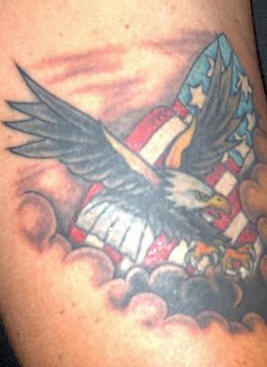 el tatuaje de color con una aguila volando con la bandera americana en las nubes