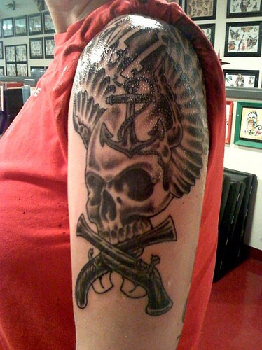 Tatuaje en el hombro Mosquetes con la ancla y el cráneo con las alas