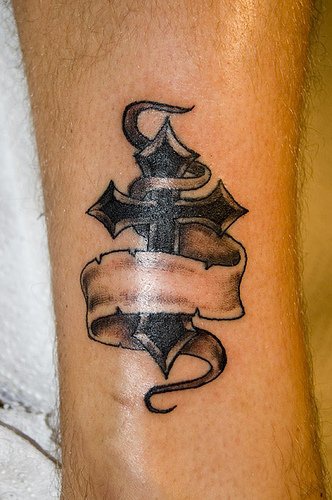 Un croix avec un ruban le tatouage sur la cheville