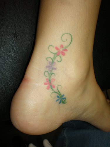 Tattoo von feiner Pflanze mit Blumen in der Knöchelgegend