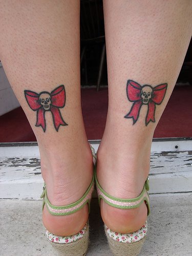 Tattoo von zwei Totenköpfen mit Schleife in der Knöchelgegend