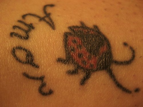 Tattoo vom Marienkäfer und Aufschrift &quotAmor" in der Knöchelgegend