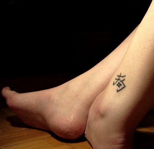 Tattoo von fremdsprachigem Buchstaben in der Knöchelgegend