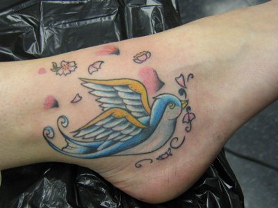 Flying blue and yellow bird ankle tattoo
