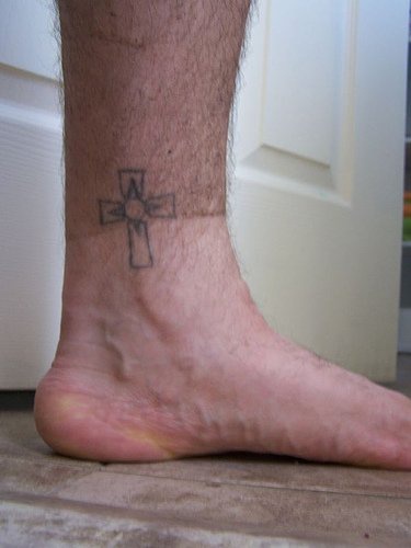 Uncolored cross ankle tattoo